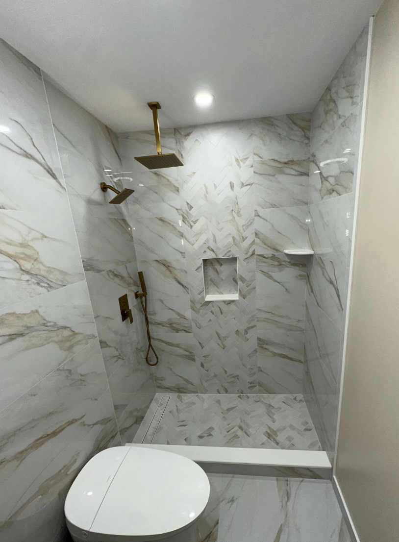 Calacatta marble walk-in shower with brass rain head and herringbone accent after remodel in Parlin, NJ